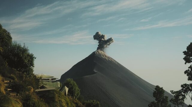 Fuego Volcano erupting with ash plume from the Acatenango hike in Guatemala. Clear morning skies, golden sunlight, striking volcanic slopes, and lush forest foreground create a vivid scene.