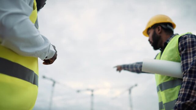 Talk of two engineers or builders against building cranes, men in helmets. Foreman on construction site, innovations and development of new district in modern city, professional builder and architect