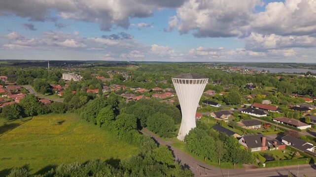 Aerial footage capturing everyday life in the suburbs of Kolding, gradually revealing the iconic mushroom-shaped water tower above residential neighborhoods and lush greenery.