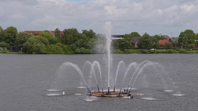 Aerial footage showcasing the iconic fountain in Kolding as the camera reveals the lakeside promenade, picturesque homes, calm water, and the beautiful cityscape of Denmark.