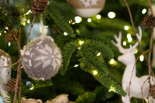 Christmas tree decorated with rustic ornaments, knitted bauble, white deer figures, pine cones and warm glowing lights, cozy festive background, natural Scandinavian holiday decor, winter celebration