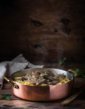 Eye Level Shot of Steaming Russian Beef Stroganoff over Egg Noodles in Copper Pan on Rustic Wood Table