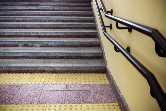 Close up of yellow tactile paving before concrete stairs with metal handrails creating barrier free environment