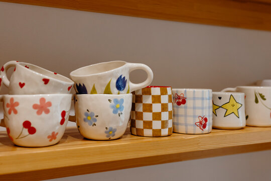 Colorful handmade ceramic mugs with playful patterns in pottery store.