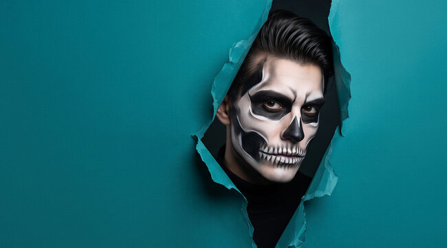 Man with skull face paint peeking through a torn hole in blue paper, looking at camera, dramatic lighting. Halloween costume, horror concept, spooky portrait, creative makeup.