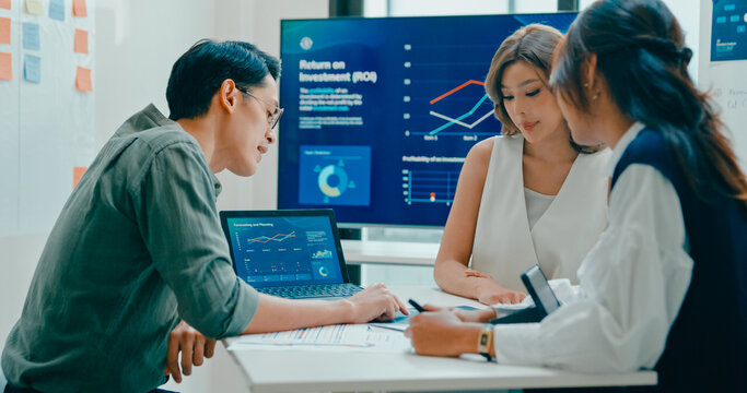 Group of Asian businesspeople work together discuss plan idea with investment data profit sale statistics in business meeting in office. Financial generation z team brainstorm on e-Commerce project.