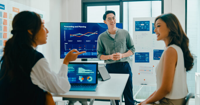 Group of Asian businesspeople work together leads business meeting uses presentation TV with revenue, profit or sale statistics in office. Financial generation z team brainstorm on e-Commerce project.