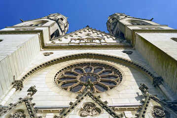 Low-angle of facade with twin towers and large rose window on Sacred Heart of Jesus Church in Timisoara. Shows impressive Neo-Gothic architecture, ecclesiastical ornamentation, and Banat heritage. © tanyatorgonskaya
