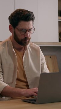 Busy Caucasian man working laptop at kitchen table thinking about financial problem typing computer male writer businessman planning project remote work indoor home office shot blurry to focused view