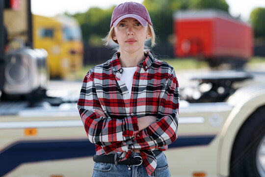 A professional truck driver poses with arms crossed in front of a heavy vehicle at a logistics depot during a bright and sunny afternoon shift