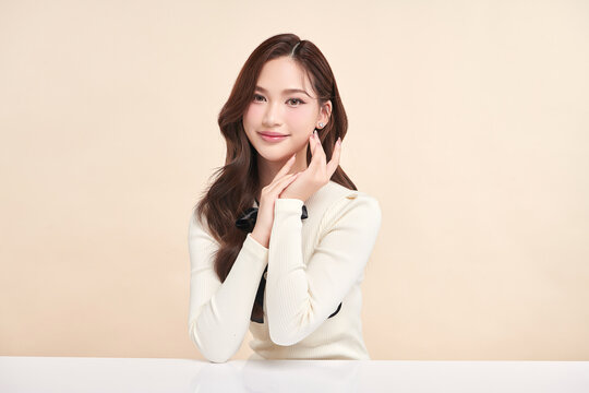 A beautiful young Asian woman with clean, fresh skin against a beige background. Skincare, facial treatment, cosmetology, beauty, and spa. An elegant portrait of an Asian woman.