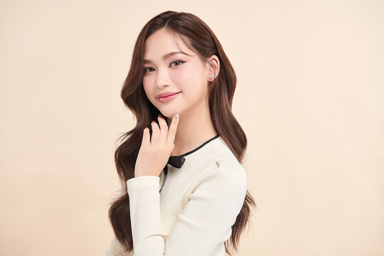 A beautiful young Asian woman with clean, fresh skin against a beige background. Skincare, facial treatment, cosmetology, beauty, and spa. An elegant portrait of an Asian woman.