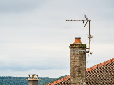 Chimney with antenna on a rooftop against cloudy sky in a town during the day