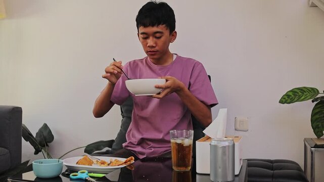 Young Asian man holding bowl and eating batagor kuah with a spoon
