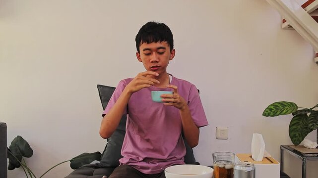 Young Asian man dipping food into sauce while eating batagor at home