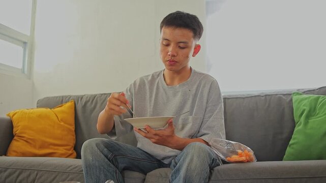 Young man eating karedok or Traditional Indonesian salad dishes and snack potato fries on sofa