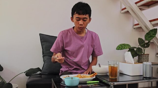 Young man eating batagor with fork while sitting in living room