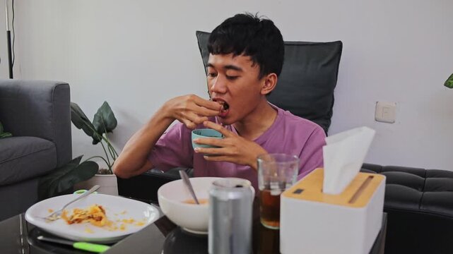 Casual moment of man eating batagor and dipping fried tofu in sauce indoors