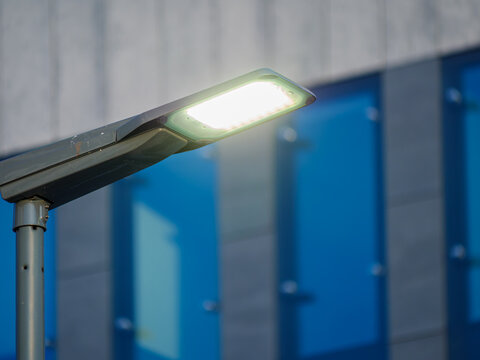 Street light shines brightly at dusk in front of a modern building