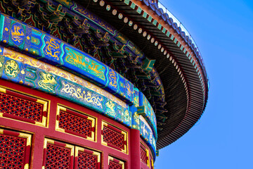 Detailed view of the ornate, colorful eaves and red lacquer walls of a traditional Chinese Imperial building against a clear blue sky. © Pei Yan