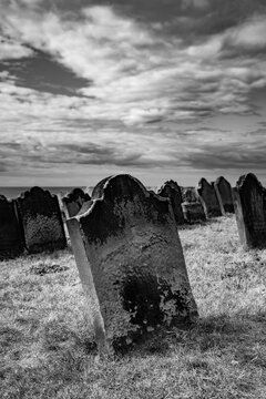 Weathered gravestone in St Mary&rsquo;s Churchyard at Whitby, North Yorkshire, overlooking the North Sea beneath a dramatic cloud-filled sky.
