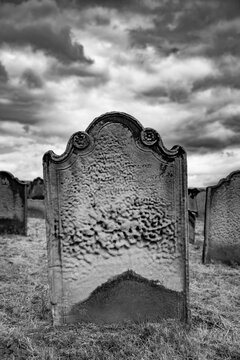 Weathered gravestone in St Mary&rsquo;s Churchyard in Whitby, North Yorkshire, beneath dramatic storm clouds, photographed in black and white with a mysterious Gothic atmosphere.