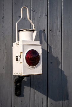 Historic white railway signal lamp with red lens at Pickering Station, North Yorkshire, photographed in bright sunlight against a dark wooden wall.