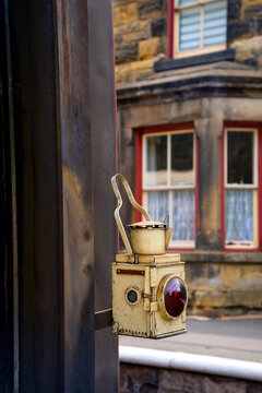 Weathered vintage signal lamp with red lens at Goathland Station in North Yorkshire, England, photographed against the softly blurred historic station building.