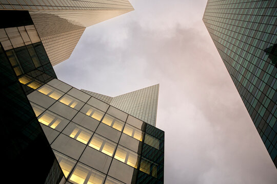 Low angle view of modern office towers in La Defense Paris France showing dramatic geometry and illuminated windows against a cloudy sky