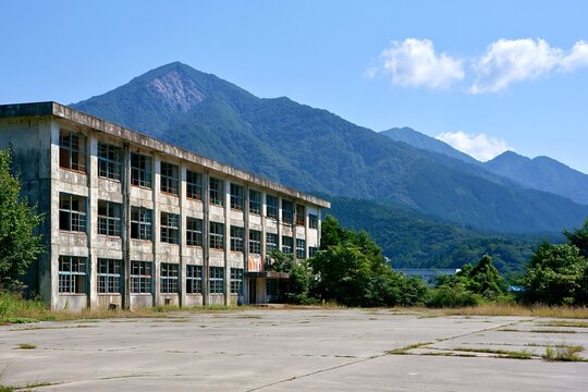 夏の青空広がる山間にある廃校舎と校庭の風景