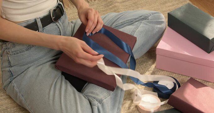 Woman hands choosing between white and blue satin ribbons putting them on gift box close up video.