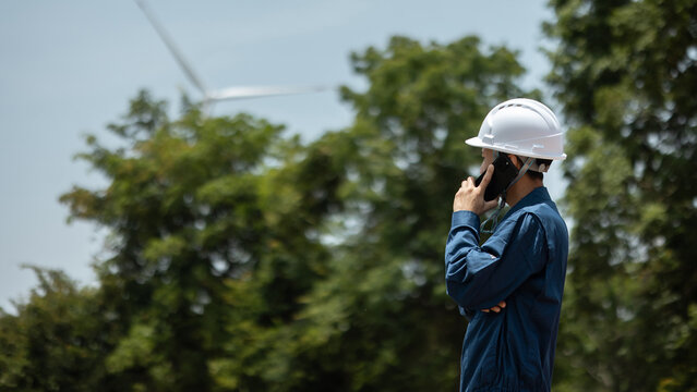 Side View of Asian Male Engineer Calling on Phone at Wind Turbine Site