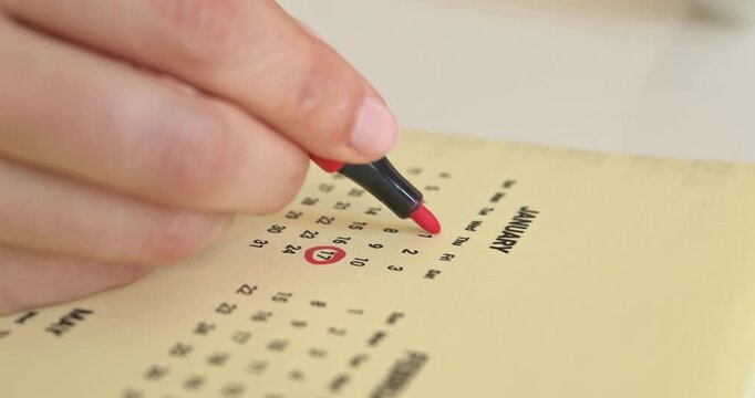 Close up of woman hand crossing out days with red marker on January calendar page.