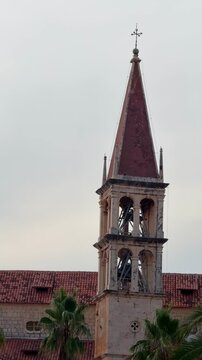 Historic church with bell tower surrounded by palm trees and shops in a sunny Mediterranean town Milna, Croatia