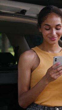 Smiling African American woman using smartphone near car trunk outdoors in city chatting online businesswoman mobile phone social media texting female driver holding coffee cup travel automobile trip