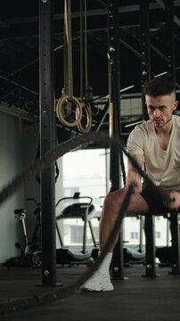 Muscular Caucasian sportsman man making waves battle ropes in gym functional workout athlete crossfit strong male guy intense training exercise sport fitness equipment strength endurance bodybuilding