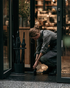 Woman kneels, tending to wet ground outside glass doors