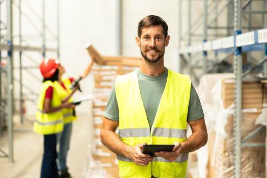 Warehouse worker standing in distribution center, holding a tablet for efficient inventory management and logistics operations