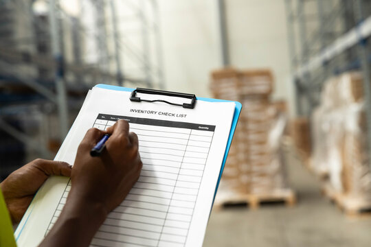 Worker writing on an inventory checklist clipboard, managing stock and logistics in a large storage warehouse