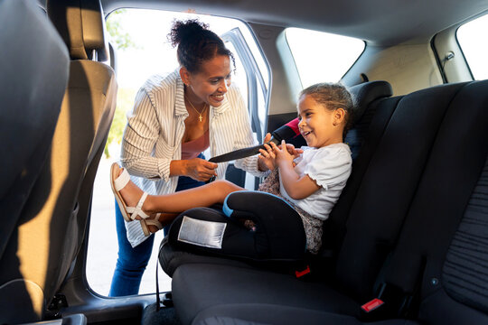 Latino mother securing child in booster seat, ensuring car safety for family travel