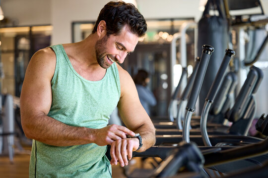 Man checking his fitness tracker at the gym. He's focused on his wearable watch, likely tracking workout stats. Office in-house gym