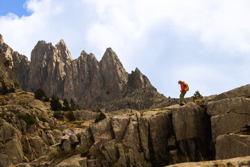 Hiker stands on rocky cliff edge. Mountain peaks tower in distance. Blue sky with clouds. Hiker shows determination. Perfect for adventure themes. Ideal for travel content © VICTOR