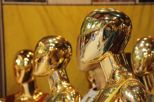 Row of futuristic golden chrome mannequins with reflective surface displayed in a clothing boutique storefront in Hoi An, Vietnam.
