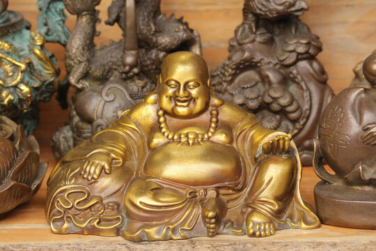 Golden brass laughing Buddha statue or Maitreya figurine displayed on a wooden shelf at a souvenir shop in Hoi An, Vietnam.