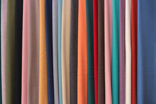 Full frame abstract texture background of various colorful textile fabric rolls hanging in a row at a tailor shop in Hoi An, Vietnam.