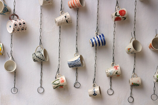 Row of colorful handmade ceramic mugs hanging on metal chains displayed outside a souvenir shop in Hoi An, Vietnam.