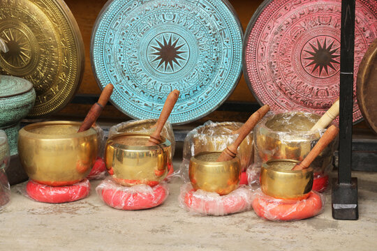 Tibetan singing bowls with wooden mallets displayed next to decorative bronze gongs at a souvenir shop in Hoi An, Vietnam.