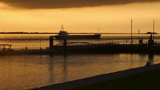 15.09.2026, Bremerhaven - Lower Saxony - Germany. Sunset over the river Weser with a ship heading to the harbour.