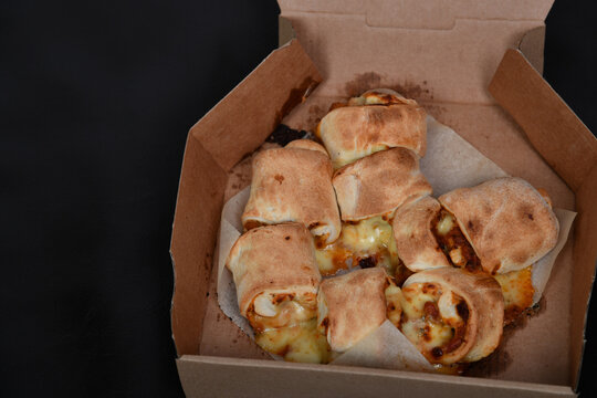 Ge&ouml;ffnete Pappbox mit herzhaften, goldbraun gebackenen Snacks auf dunkler Sitzfl&auml;che. Fingerfood, Take-away, Partyfood, Imbiss, Lieferservice und authentische Food-Fotografie. pizza b&auml;llchen pizza roo