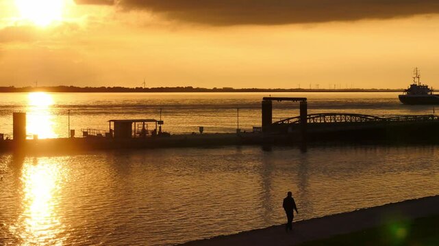 15.09.2026, Bremerhaven - Lower Saxony - Germany. Sunset over the river Weser, man taking an evening stroll.